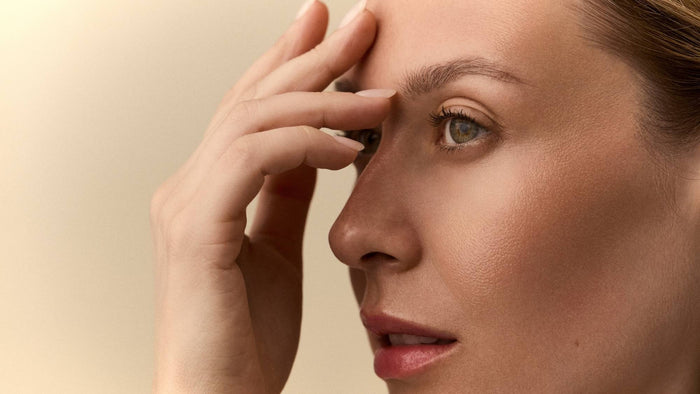 Close-up side profile of a person gently touching the skin around their forehead and eye.